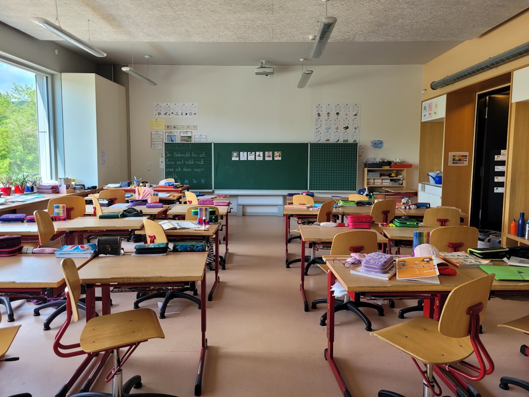 An empty elementary classroom with student desks, chairs, and a chalkboard at the front of the room