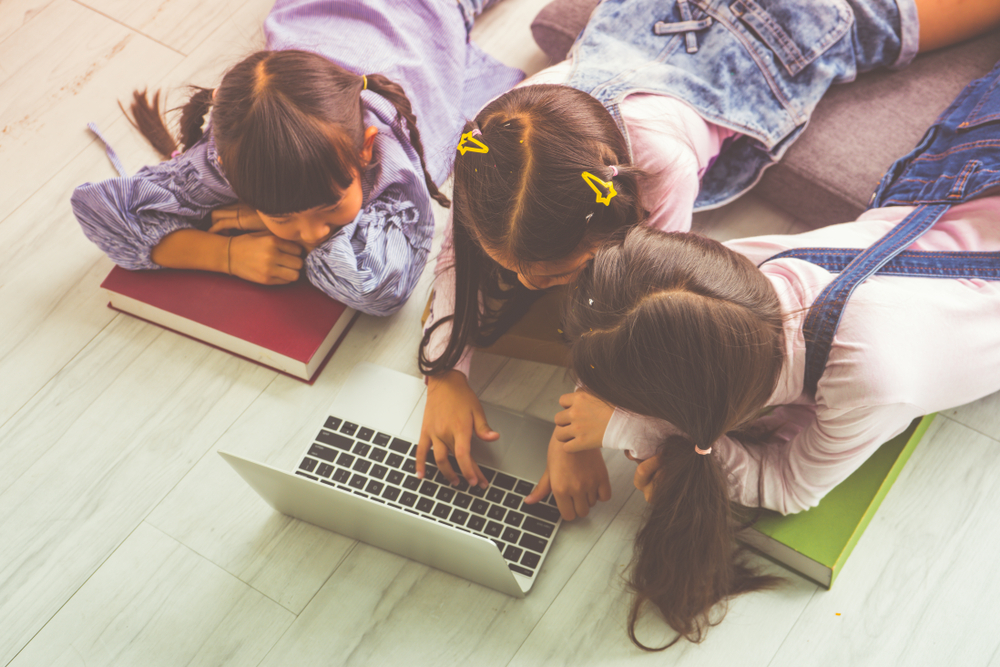 Three young students gathered around a laptop, learning together